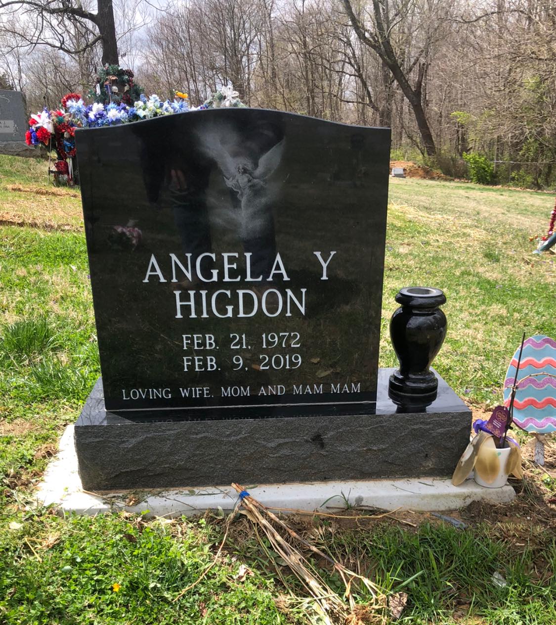 Black granite memorial stone with angel motif in a wooded cemetery setting